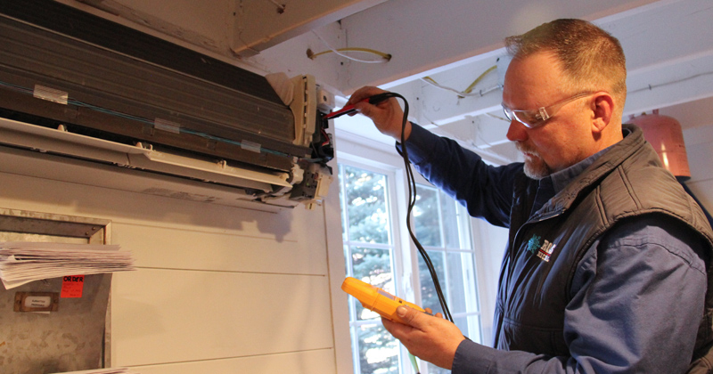 Technician from Rolls Mechanical works on an air conditioner